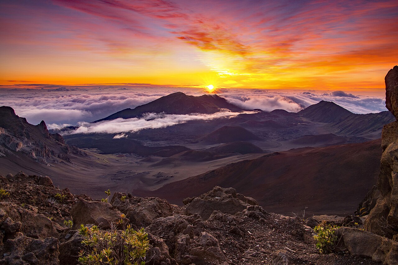 A brilliant orange sunrise bursting over a sea of white trade-wind inversion clouds viewed from the 10,023-foot volcanic rim of Haleakala