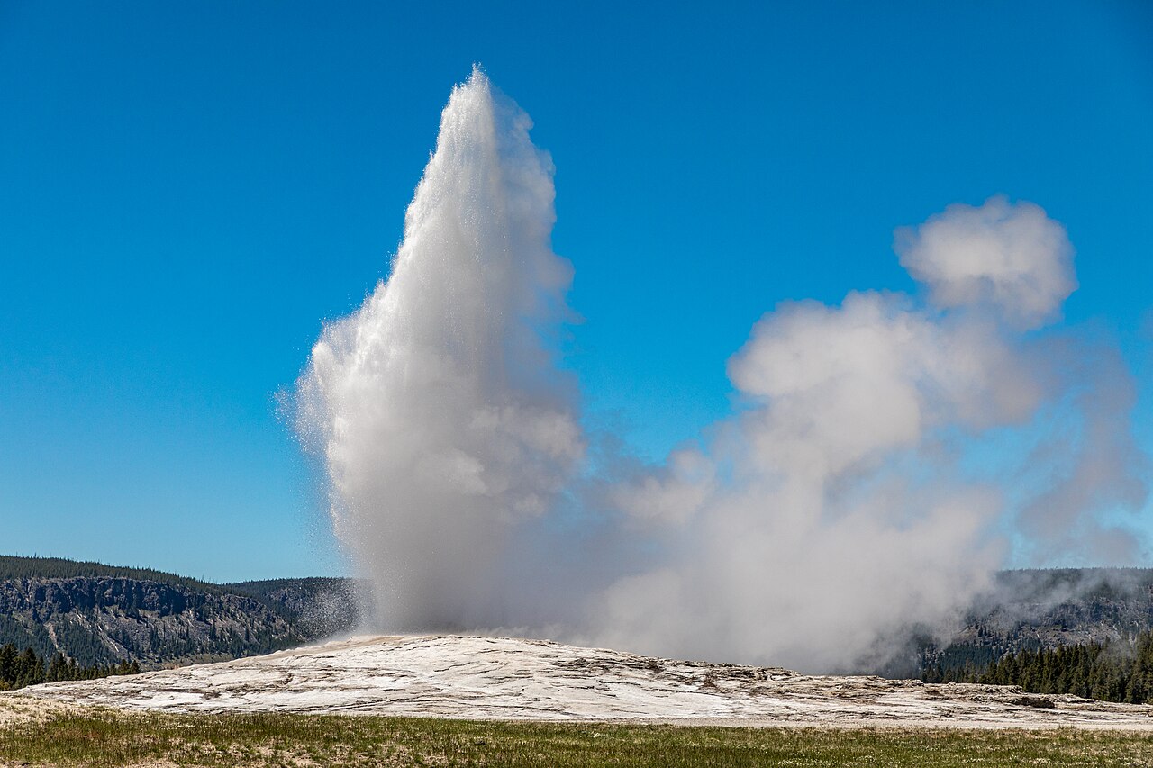 Old Faithful geyser erupting a towering column of steam and boiling water into a blue sky in Yellowstone National Park