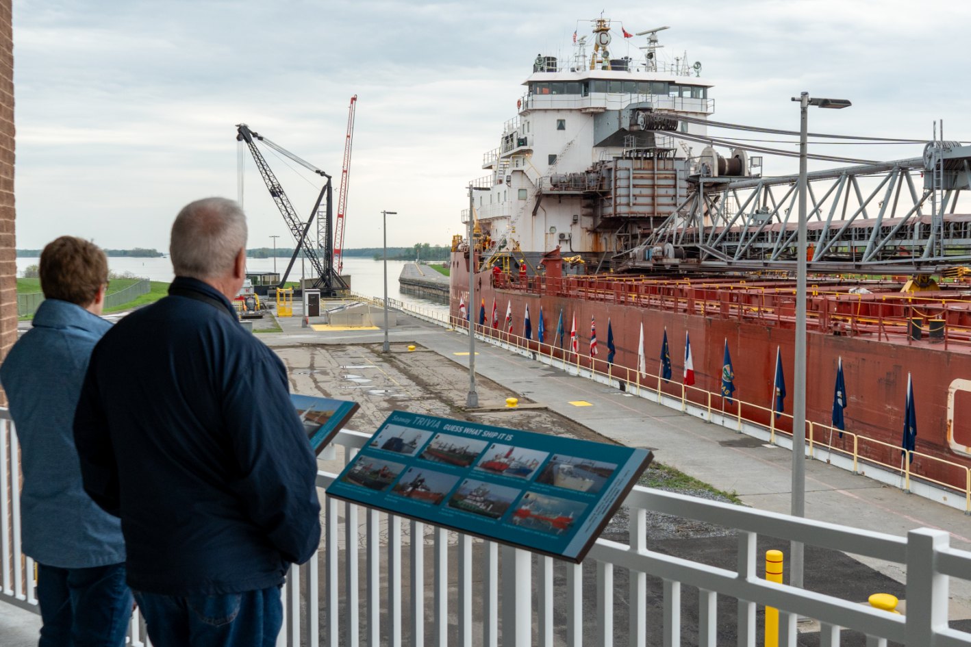 Visitors on the Eisenhower Lock observation deck looking at a red freighter in the chamber