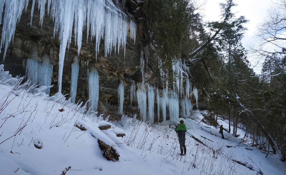 A person beside large blue ice curtains at Pictured Rocks in a National Park Service reference photograph